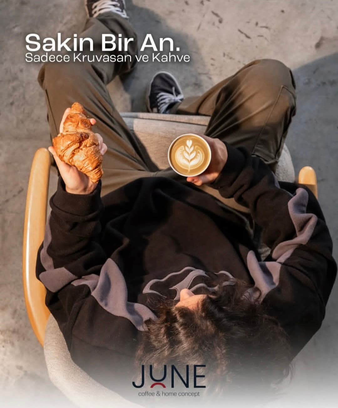 June Coffee için çekilmiş, kruvasan ve latte tutan kişinin yukarıdan görüntüsü